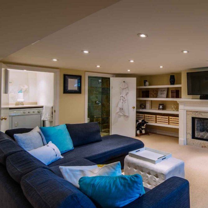 A refinished basement with modern blue couches and fireplace.